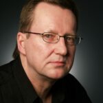 Close-up portrait of a serious businessman in eyeglasses against a dark background.